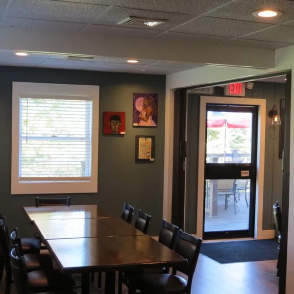 A long wooden dining table with chairs in a restaurant, with a window and exit door to a deck.