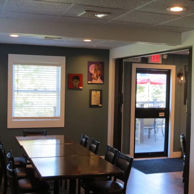 A long wooden dining table with chairs in a restaurant, with a window and exit door to a deck.