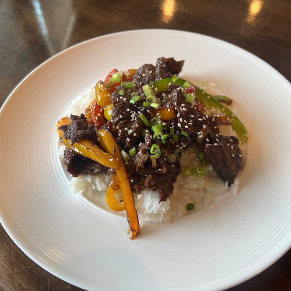 Beef stir-fry with bell peppers, sesame seeds, and scallions over white rice on a white plate.