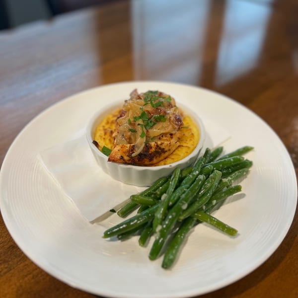Grilled chicken with caramelized onions on polenta, served with green beans on a white plate.