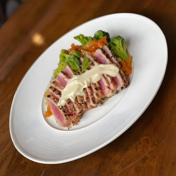 Seared tuna with a creamy sauce, broccoli, and carrots on a white oval plate at Tick Tock's.
