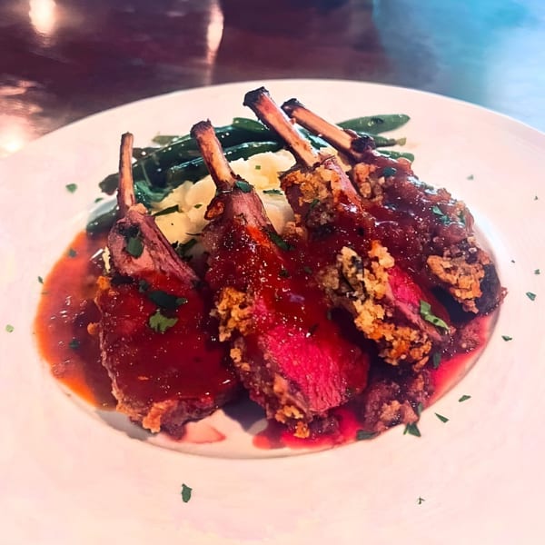 Four lamb chops with a red sauce, mashed potatoes, and green beans on a white plate.