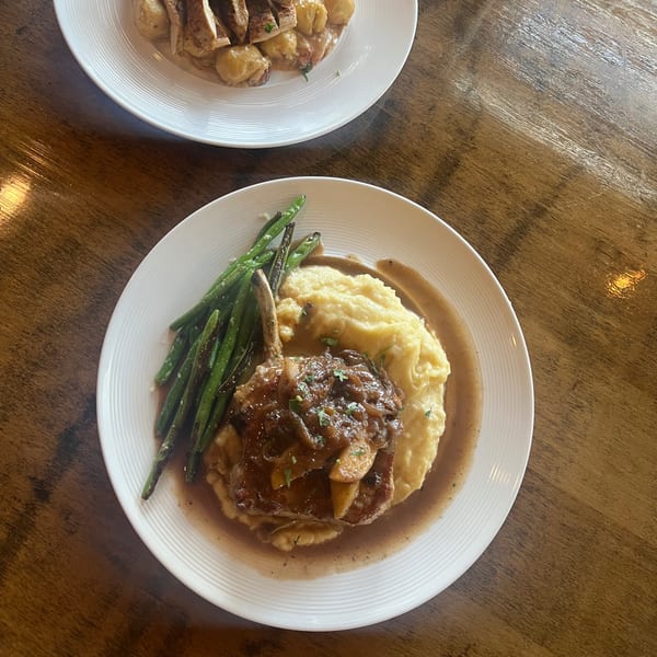 Pork chop with mashed potatoes, gravy, and green beans on a white plate at Tick Tock's on Terrace.