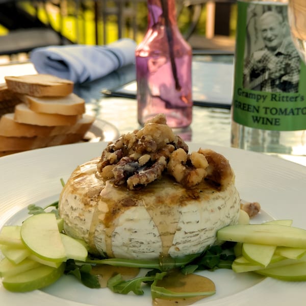Baked brie with walnuts, honey, green apple slices, and arugula, served with bread and wine.