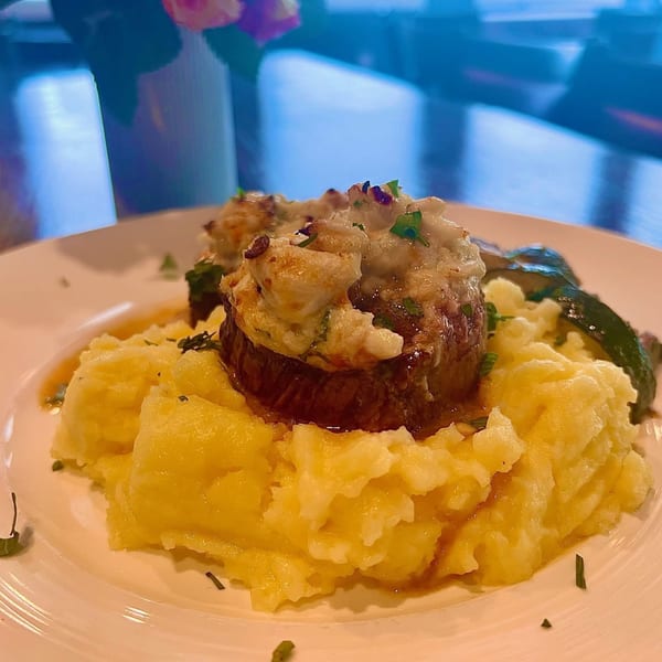 A steak topped with crab meat and cheese, served over mashed potatoes with a side of green beans.